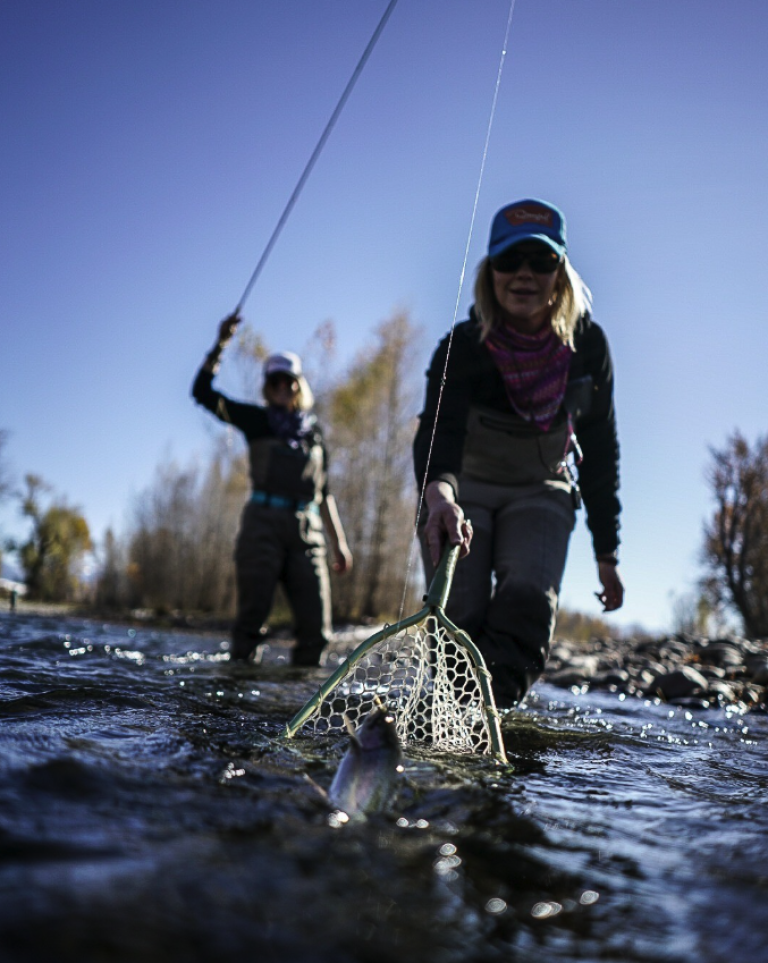fishing guide netting a brown trout on the madison river in montana